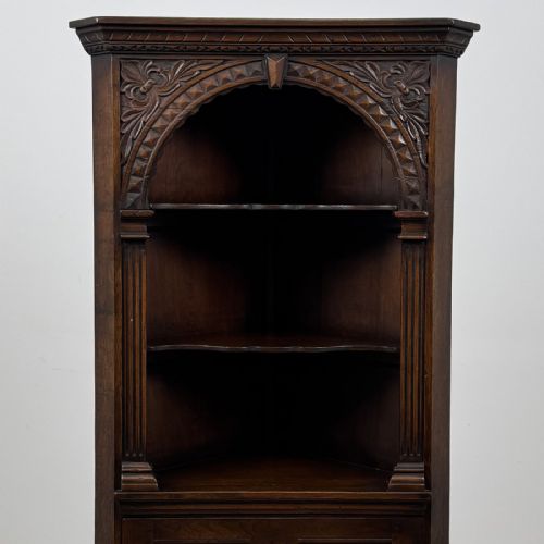 fig 4. A tall dark oak Jacobean style corner cabinet featuring an upper open section with an arched alcove and two shelves above a single panelled cupboard door.