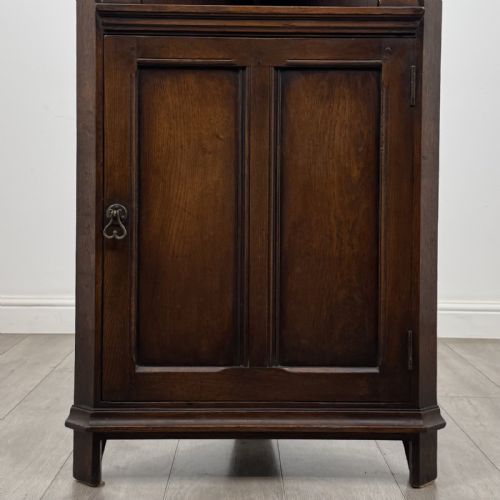 fig 5. A tall dark oak Jacobean style corner cabinet featuring an upper open section with an arched alcove and two shelves above a single panelled cupboard door.
