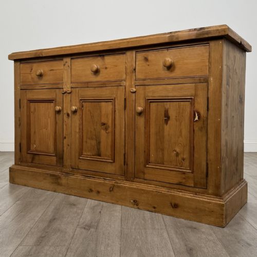 fig 1. A vintage natural pine sideboard featuring three top drawers above three panelled cupboard doors with turned wooden knobs and a solid plinth base.
