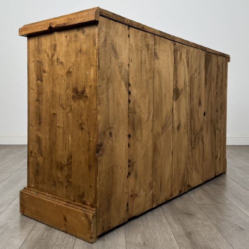 fig 3. A vintage natural pine sideboard featuring three top drawers above three panelled cupboard doors with turned wooden knobs and a solid plinth base.