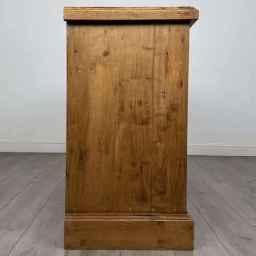fig 6. A vintage natural pine sideboard featuring three top drawers above three panelled cupboard doors with turned wooden knobs and a solid plinth base.