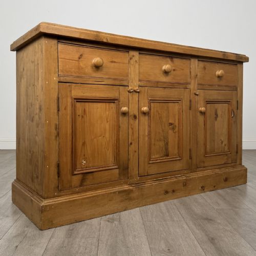 fig 7. A vintage natural pine sideboard featuring three top drawers above three panelled cupboard doors with turned wooden knobs and a solid plinth base.