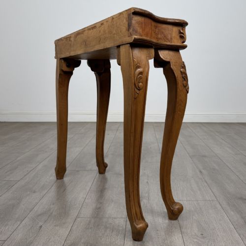 fig 5. A light oak French-style console table featuring a serpentine front, carved relief details on the apron, and cabriole legs.