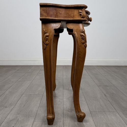 fig 6. A light oak French-style console table featuring a serpentine front, carved relief details on the apron, and cabriole legs.
