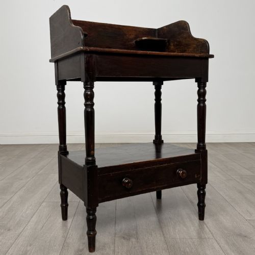 fig 7. A dark stained Victorian pine washstand featuring a three-quarter gallery back, turned legs, a lower shelf, and a base drawer with two turned wooden knobs.