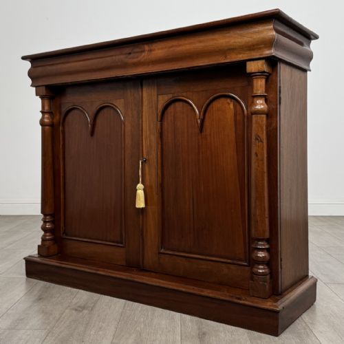 fig 1. An antique Victorian dark mahogany side cabinet featuring double arched panel doors, flanking turned columns, a plinth base, and a concealed frieze drawer.