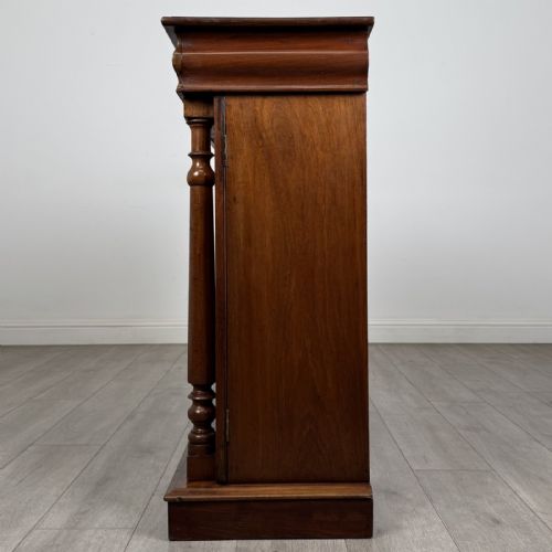 fig 2. An antique Victorian dark mahogany side cabinet featuring double arched panel doors, flanking turned columns, a plinth base, and a concealed frieze drawer.