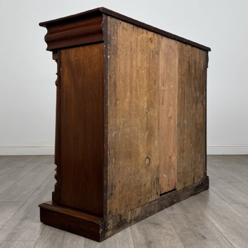 fig 3. An antique Victorian dark mahogany side cabinet featuring double arched panel doors, flanking turned columns, a plinth base, and a concealed frieze drawer.