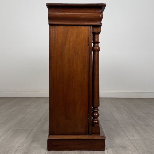 fig 6. An antique Victorian dark mahogany side cabinet featuring double arched panel doors, flanking turned columns, a plinth base, and a concealed frieze drawer.