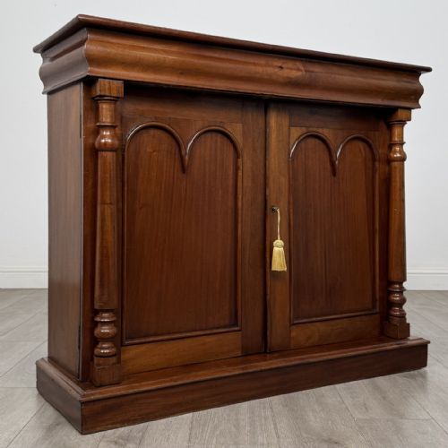 fig 7. An antique Victorian dark mahogany side cabinet featuring double arched panel doors, flanking turned columns, a plinth base, and a concealed frieze drawer.