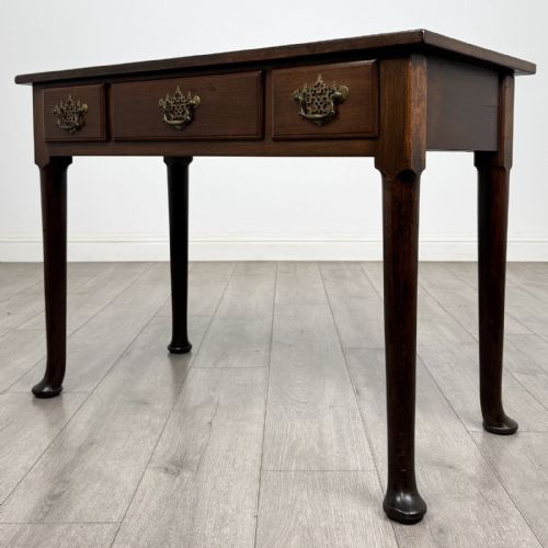 fig 1. A dark mahogany Georgian style side table featuring three drawers with ornamental brass handles and four tapered legs with pad feet.