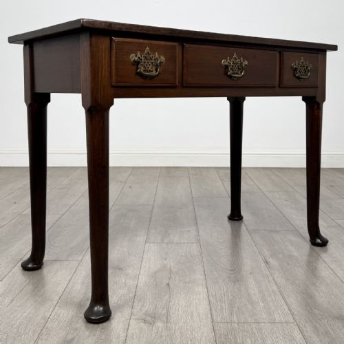 fig 7. A dark mahogany Georgian style side table featuring three drawers with ornamental brass handles and four tapered legs with pad feet.
