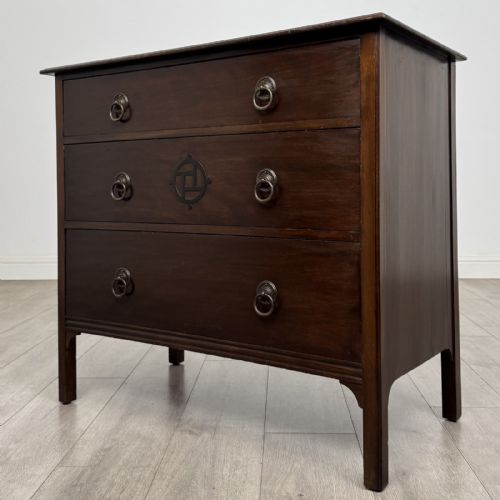 fig 1. A dark mahogany Arts and Crafts chest of drawers with three drawers, circular brass ring handles, and a central circular motif.