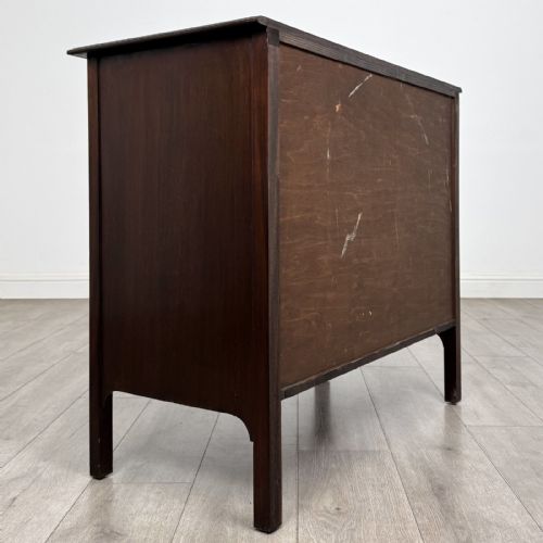 fig 3. A dark mahogany Arts and Crafts chest of drawers with three drawers, circular brass ring handles, and a central circular motif.