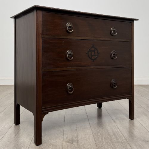 fig 7. A dark mahogany Arts and Crafts chest of drawers with three drawers, circular brass ring handles, and a central circular motif.