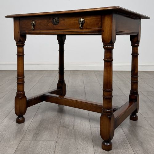 fig 1. A warm brown fruitwood side table featuring a single drawer with twin brass drop handles, turned legs, and an H-stretcher.
