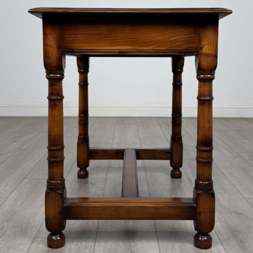fig 2. A warm brown fruitwood side table featuring a single drawer with twin brass drop handles, turned legs, and an H-stretcher.