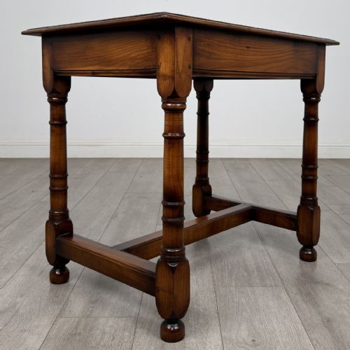 fig 3. A warm brown fruitwood side table featuring a single drawer with twin brass drop handles, turned legs, and an H-stretcher.