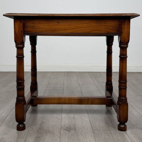 fig 4. A warm brown fruitwood side table featuring a single drawer with twin brass drop handles, turned legs, and an H-stretcher.