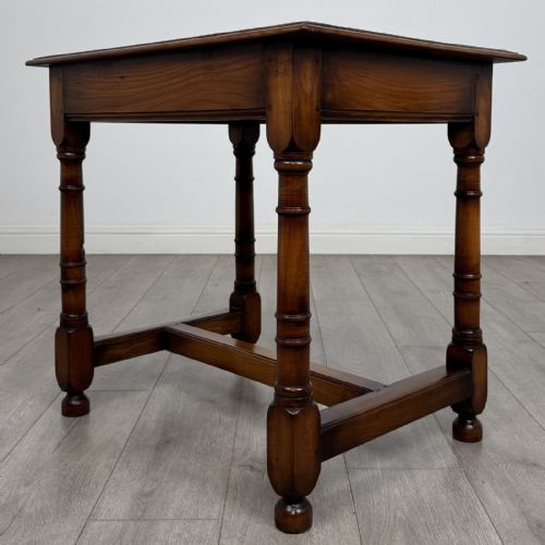 fig 5. A warm brown fruitwood side table featuring a single drawer with twin brass drop handles, turned legs, and an H-stretcher.