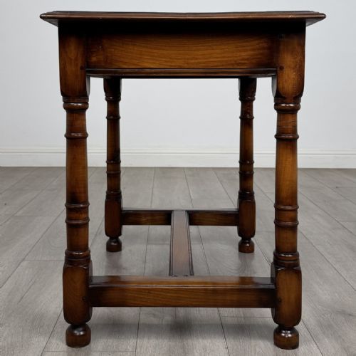 fig 6. A warm brown fruitwood side table featuring a single drawer with twin brass drop handles, turned legs, and an H-stretcher.