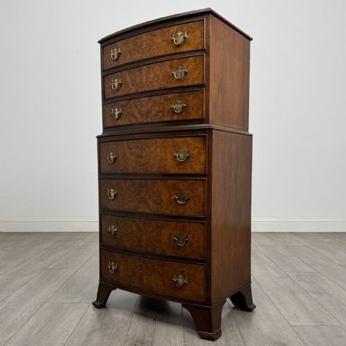 fig 1. A Georgian style burr walnut tallboy featuring a bow-front silhouette, seven stacked drawers with brass handles, and bracket feet.
