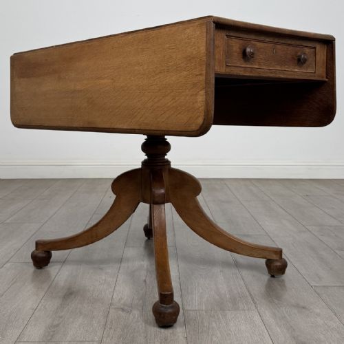 fig 2. A 19th-century solid oak Pembroke table with drop-down leaves, a single frieze drawer with turned wooden knobs, and a turned pedestal supported by four splayed sabre legs.