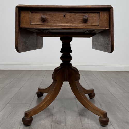 fig 3. A 19th-century solid oak Pembroke table with drop-down leaves, a single frieze drawer with turned wooden knobs, and a turned pedestal supported by four splayed sabre legs.