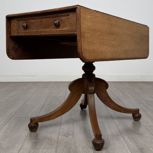 fig 4. A 19th-century solid oak Pembroke table with drop-down leaves, a single frieze drawer with turned wooden knobs, and a turned pedestal supported by four splayed sabre legs.