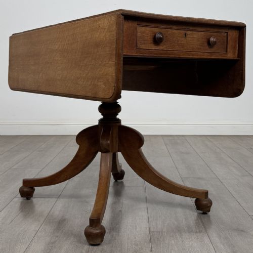 fig 6. A 19th-century solid oak Pembroke table with drop-down leaves, a single frieze drawer with turned wooden knobs, and a turned pedestal supported by four splayed sabre legs.