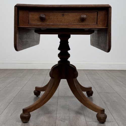 fig 7. A 19th-century solid oak Pembroke table with drop-down leaves, a single frieze drawer with turned wooden knobs, and a turned pedestal supported by four splayed sabre legs.