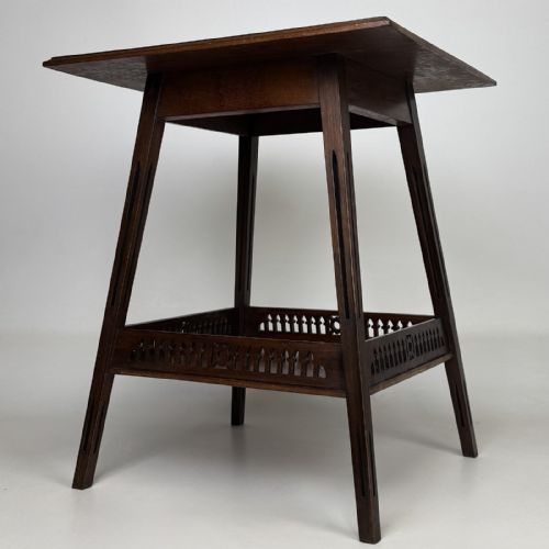 fig 1. An Edwardian dark mahogany lamp table featuring splayed legs with elongated vertical cutouts and a lower shelf enclosed by a carved fretwork gallery.