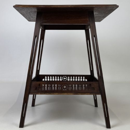 fig 2. An Edwardian dark mahogany lamp table featuring splayed legs with elongated vertical cutouts and a lower shelf enclosed by a carved fretwork gallery.