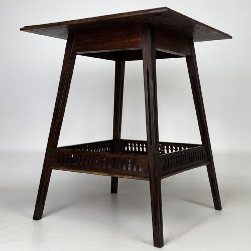 fig 3. An Edwardian dark mahogany lamp table featuring splayed legs with elongated vertical cutouts and a lower shelf enclosed by a carved fretwork gallery.