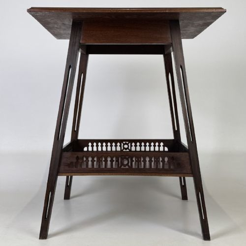 fig 4. An Edwardian dark mahogany lamp table featuring splayed legs with elongated vertical cutouts and a lower shelf enclosed by a carved fretwork gallery.