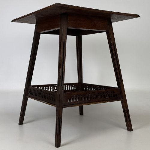fig 5. An Edwardian dark mahogany lamp table featuring splayed legs with elongated vertical cutouts and a lower shelf enclosed by a carved fretwork gallery.