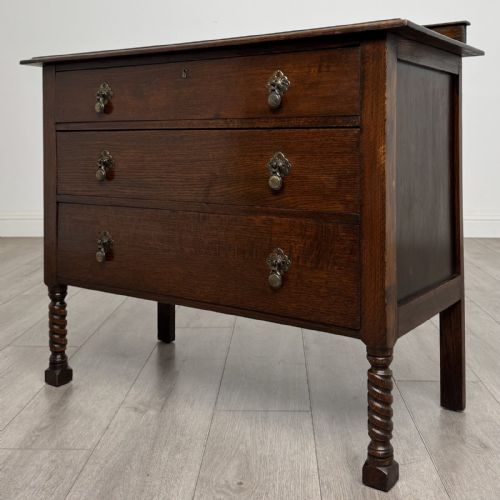 fig 1. A dark oak chest of drawers featuring three full-width drawers with metal drop handles and front barley twist legs.