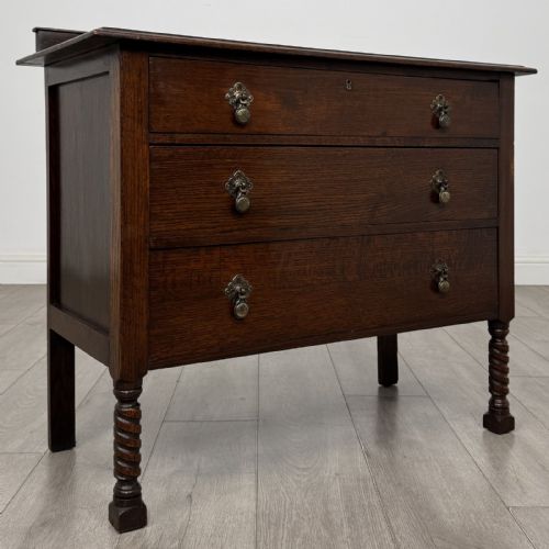 fig 7. A dark oak chest of drawers featuring three full-width drawers with metal drop handles and front barley twist legs.