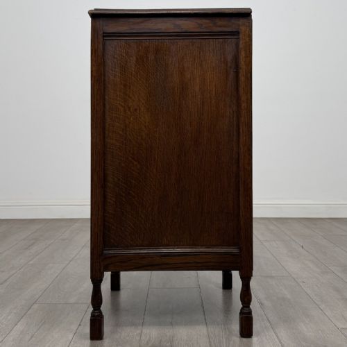 fig 2. A dark brown oak record cabinet featuring a single panelled door with a brass knob and turned legs.