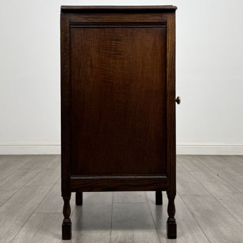 fig 6. A dark brown oak record cabinet featuring a single panelled door with a brass knob and turned legs.