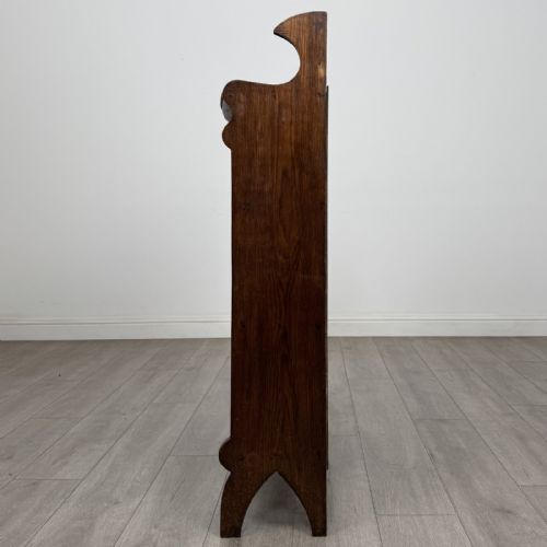fig 3. An Arts and Crafts dark oak open bookcase featuring three shelves, a light blue painted back panel, and a carved cresting gallery.