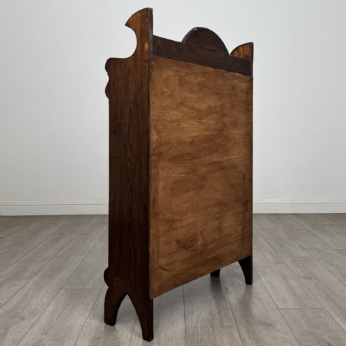 fig 4. An Arts and Crafts dark oak open bookcase featuring three shelves, a light blue painted back panel, and a carved cresting gallery.