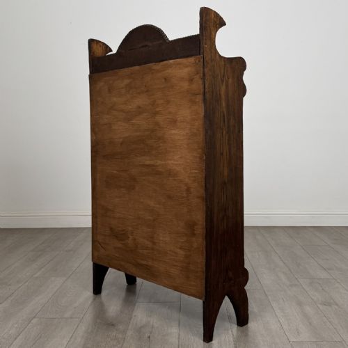 fig 6. An Arts and Crafts dark oak open bookcase featuring three shelves, a light blue painted back panel, and a carved cresting gallery.