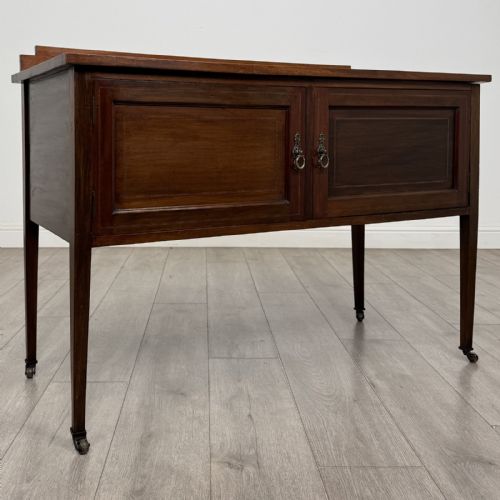fig 7. An Edwardian mahogany side cabinet featuring double panelled doors with line inlay, square tapered legs, brass drop handles, and brass castors.