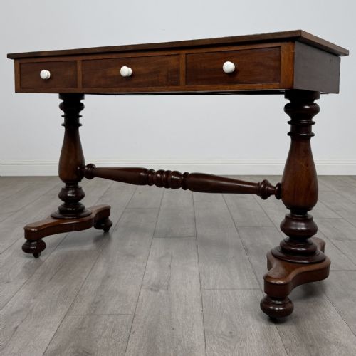 fig 1. A Victorian mahogany writing table featuring three front drawers with white porcelain knobs, set on turned baluster legs with a central stretcher bar and castors.