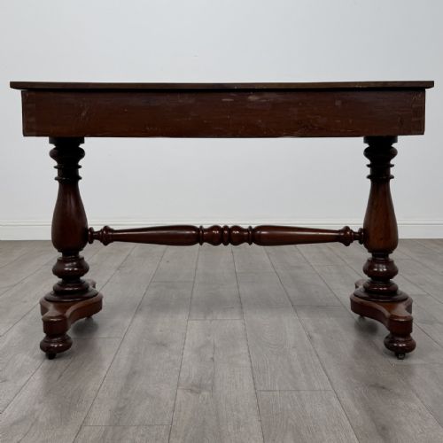fig 4. A Victorian mahogany writing table featuring three front drawers with white porcelain knobs, set on turned baluster legs with a central stretcher bar and castors.