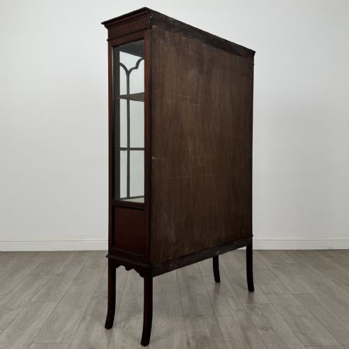 fig 4. An Edwardian mahogany display cabinet featuring two astragal glazed doors, a shaped arched cresting, and lower veneered panels supported on slender splayed legs.