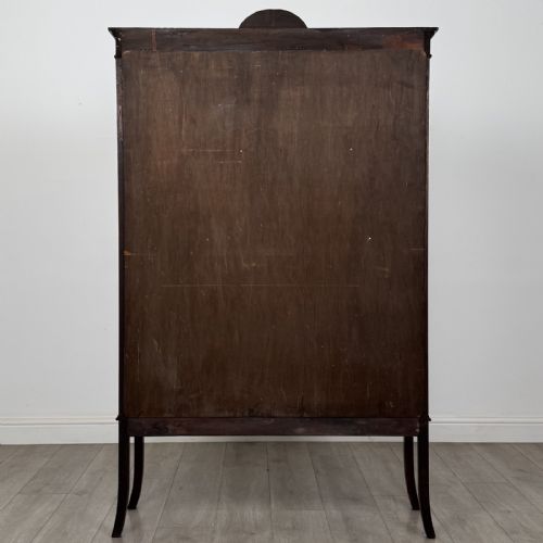 fig 5. An Edwardian mahogany display cabinet featuring two astragal glazed doors, a shaped arched cresting, and lower veneered panels supported on slender splayed legs.