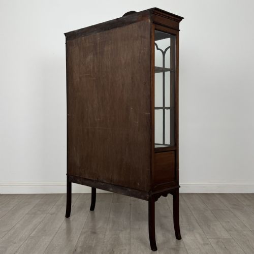 fig 6. An Edwardian mahogany display cabinet featuring two astragal glazed doors, a shaped arched cresting, and lower veneered panels supported on slender splayed legs.