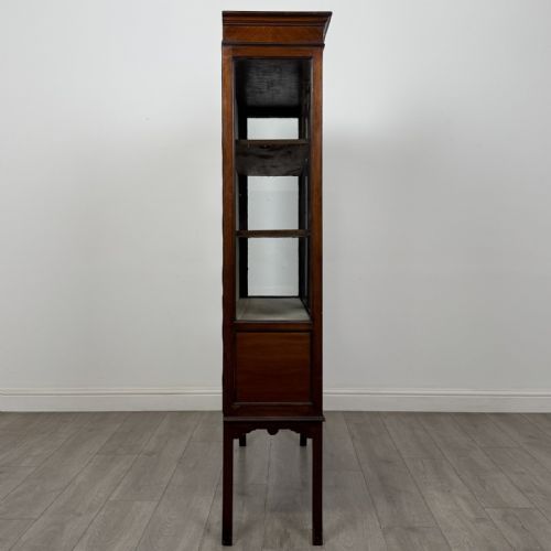 fig 7. An Edwardian mahogany display cabinet featuring two astragal glazed doors, a shaped arched cresting, and lower veneered panels supported on slender splayed legs.